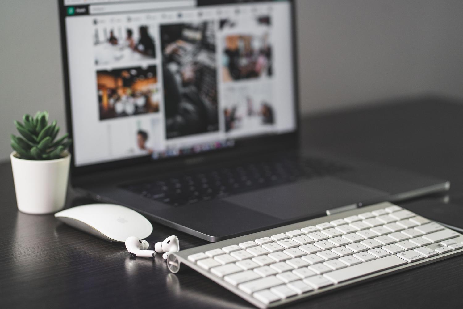 Primer plano de un teclado y ratón modernos en un escritorio blanco con una planta, evocando un entorno de trabajo eficiente y organizado.