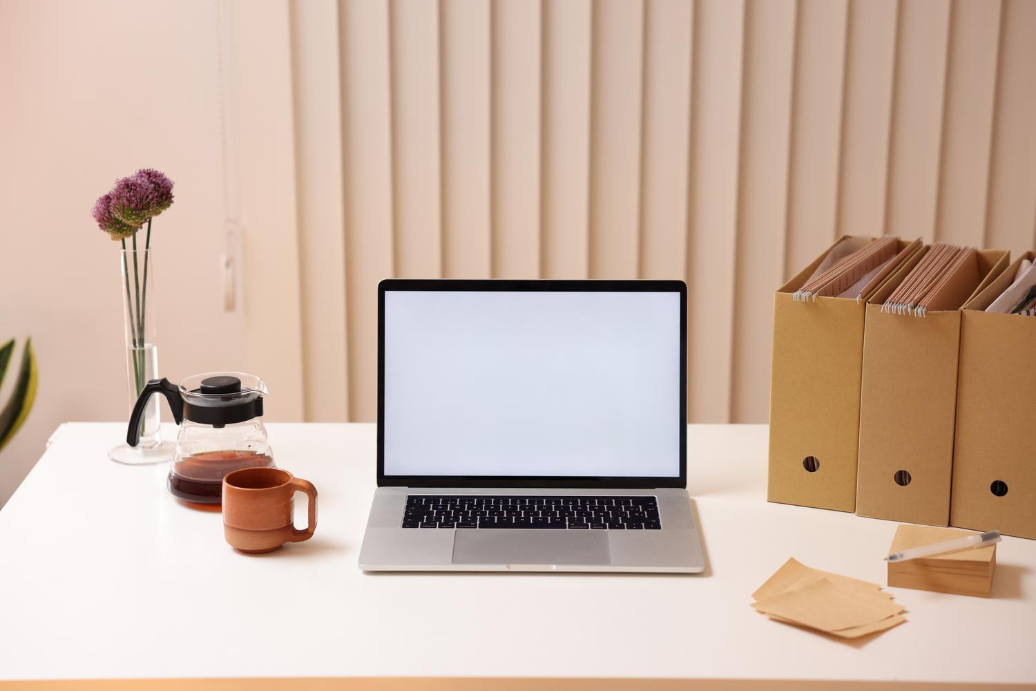 Espacio de trabajo minimalista con ordenador portátil y organizadores de archivos, representando la organización de archivos digitales.