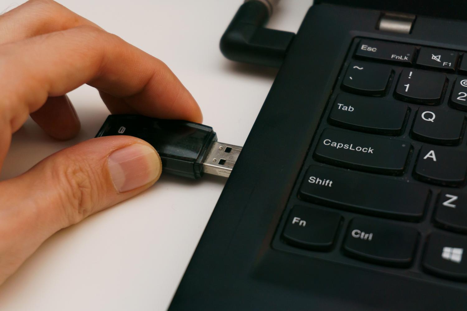 Primer plano detallado de una memoria USB siendo insertada en un puerto de portátil sobre un fondo blanco y limpio.