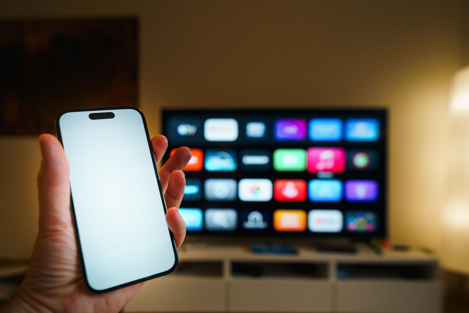 Smartphone en primer plano con una Smart TV de fondo, mostrando la conectividad y el ecosistema entre el móvil y la televisión.