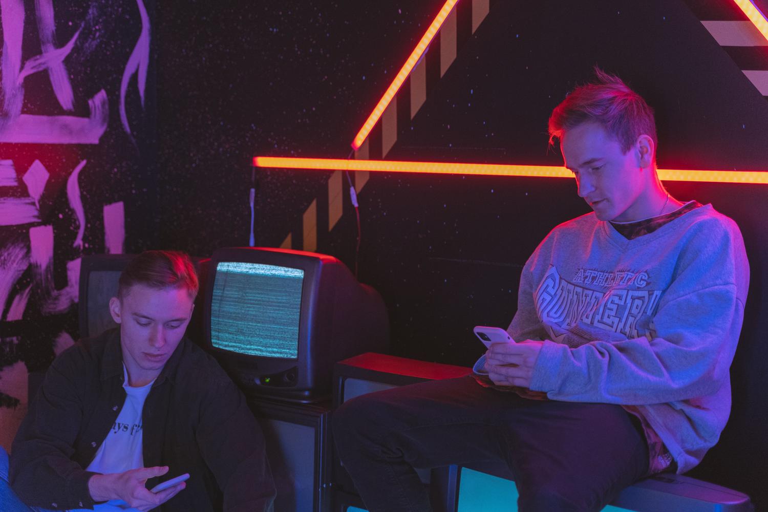 Jóvenes utilizando smartphones en un entorno gaming con luces neón y televisores, evocando una atmósfera de juego multijugador inalámbrico.