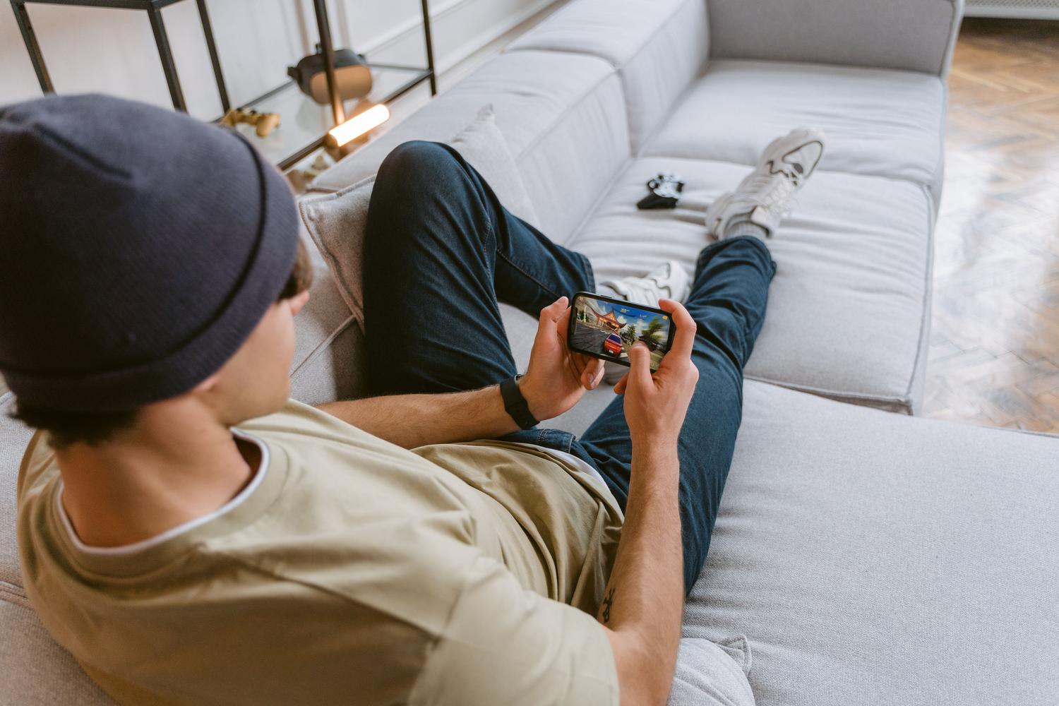 Persona relajada en un sofá utilizando un smartphone en posición horizontal para jugar, representando el uso de un mando virtual para Google TV.