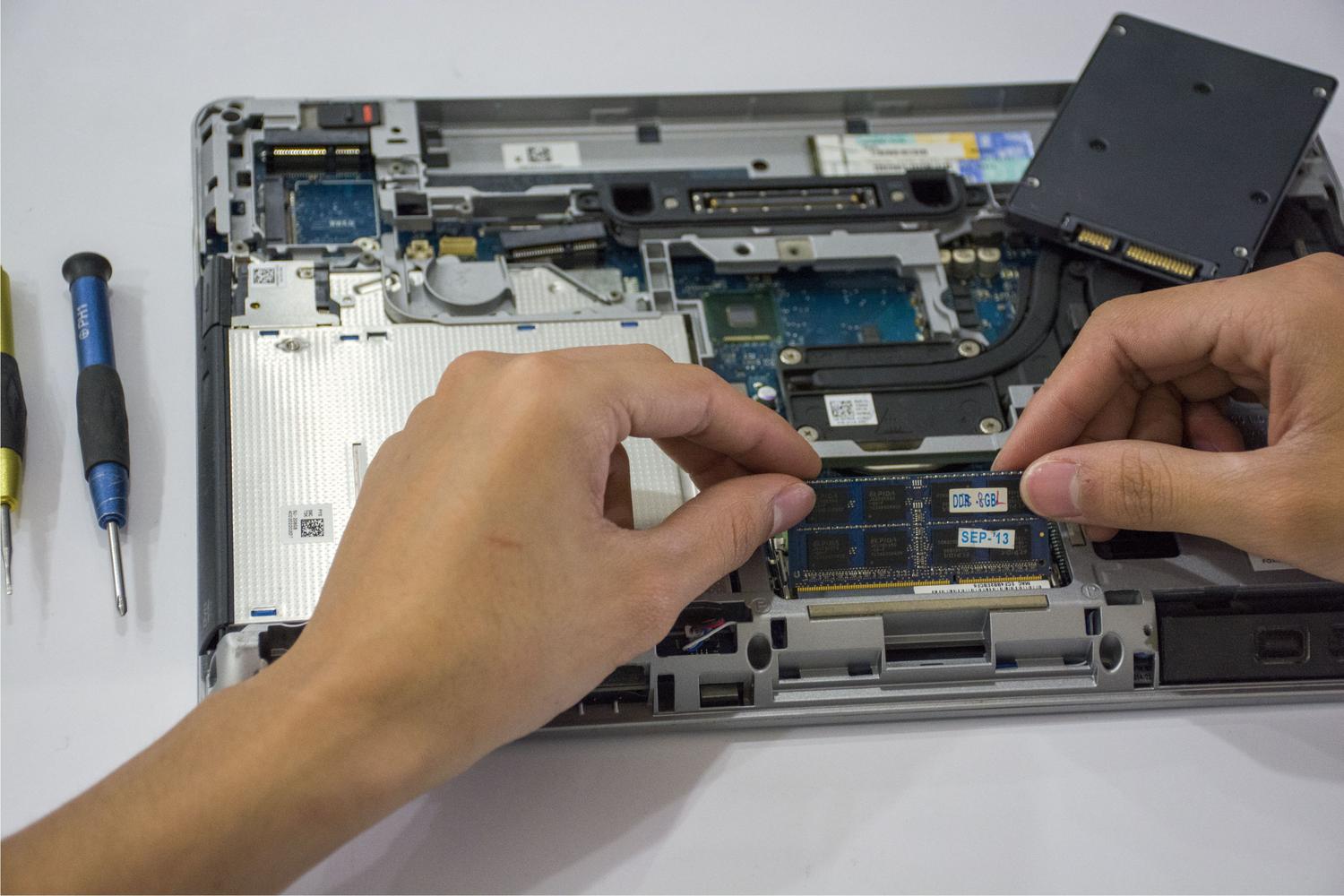 Técnico profesional instalando un módulo de memoria RAM en la placa base de un portátil.