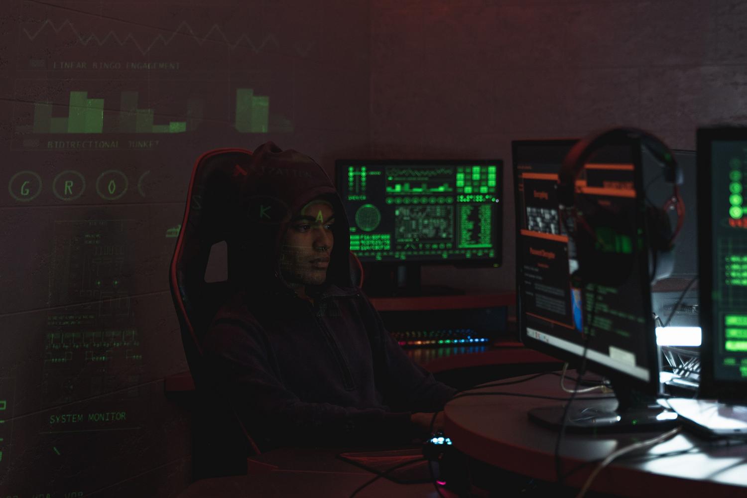 Ciberdelincuente con capucha trabajando con múltiples monitores en una habitación oscura, simbolizando el ataque a redes internas.
