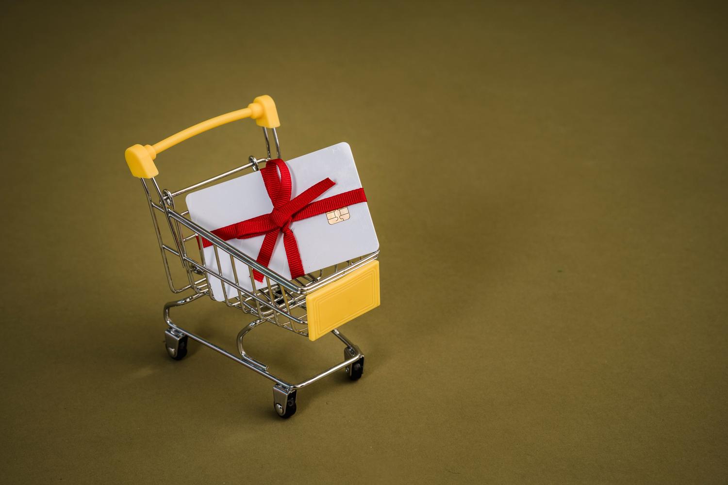 Tarjeta de regalo con un lazo rojo en un mini carrito de compras sobre fondo neutro, simbolizando el canje de premios.