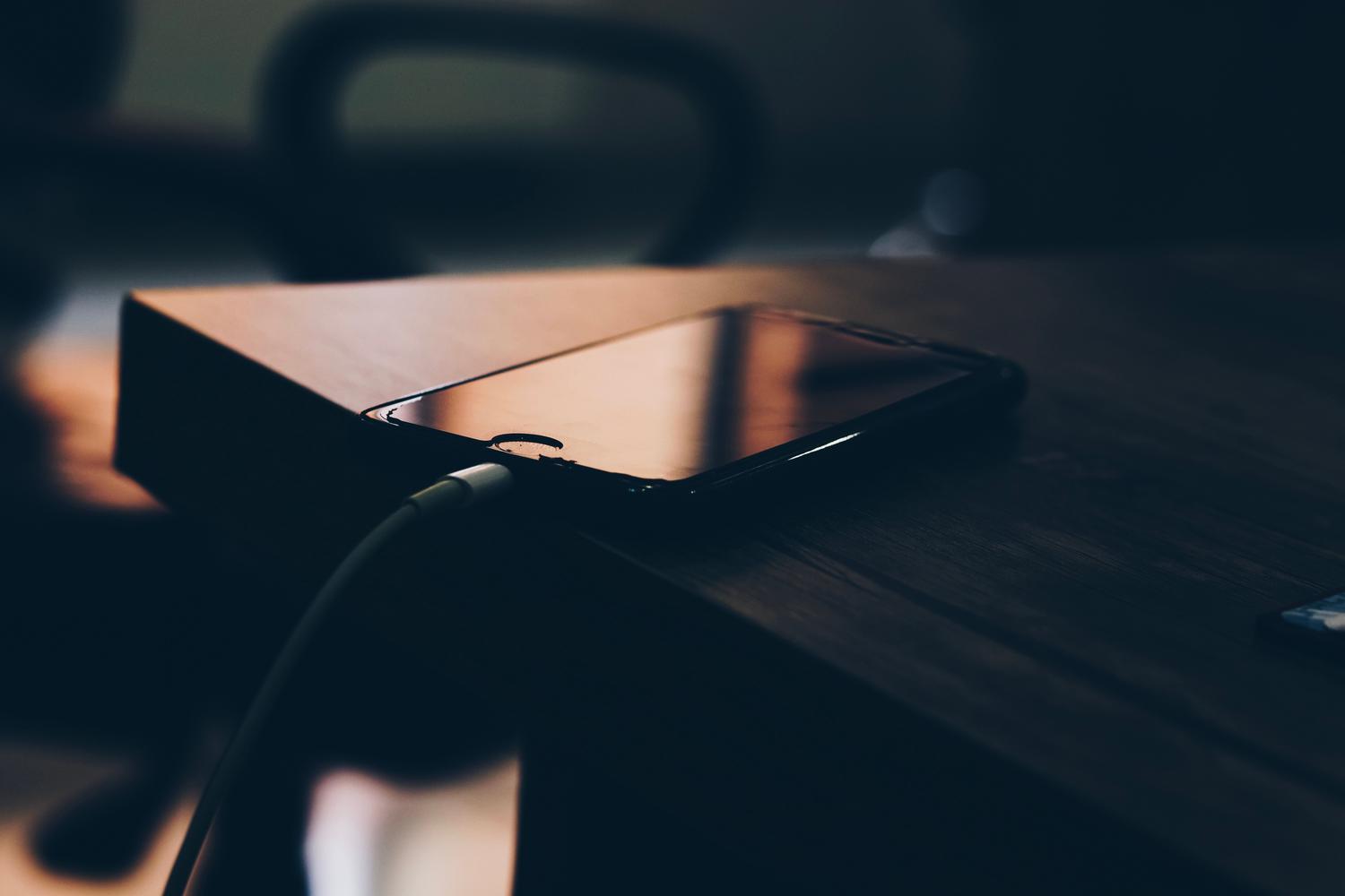 Smartphone conectado a un cargador sobre una mesa de madera, ilustrando el modo de protector de pantalla en Android.