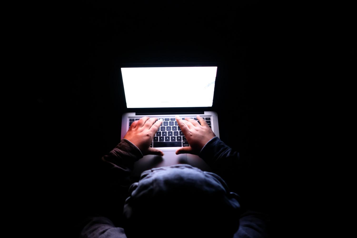 Silueta de una persona usando un portátil en una habitación oscura, representando el riesgo de intrusos y la vulnerabilidad de la red.