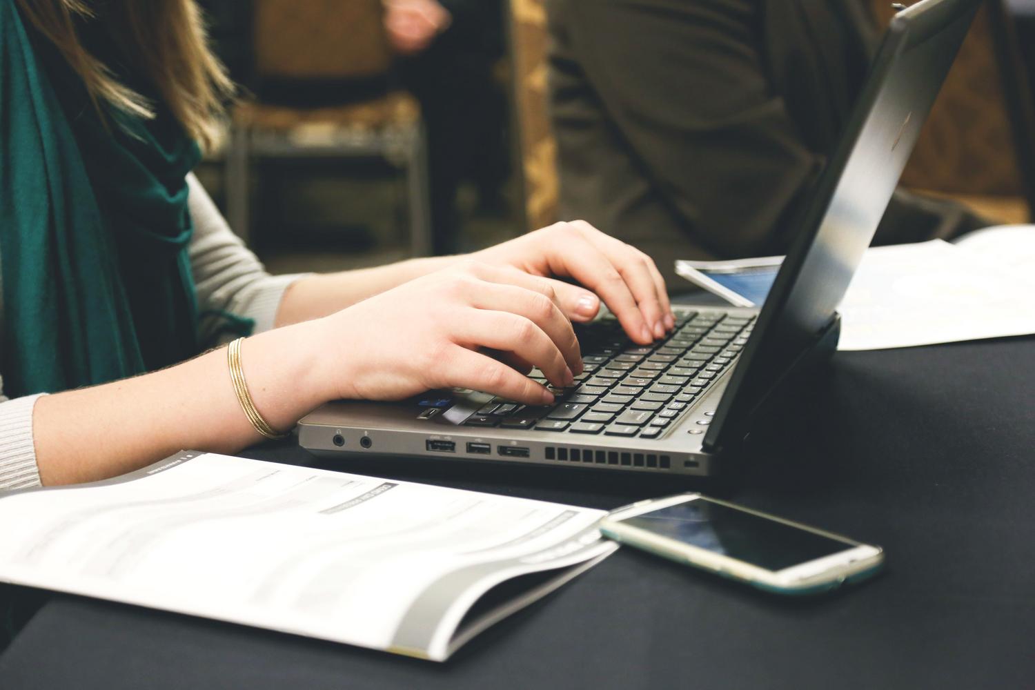 Mujer trabajando en un portátil junto a documentos físicos, mostrando la transición entre el mundo analógico y la gestión digital de PDFs.