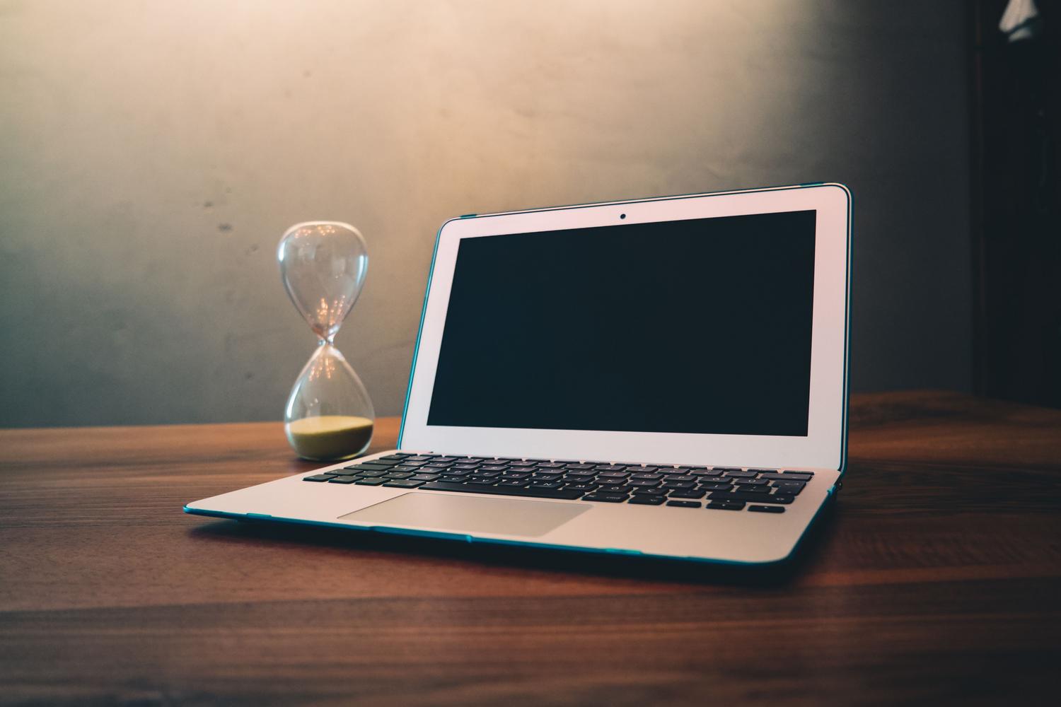 Laptop junto a un reloj de arena, simbolizando la ralentización del sistema, el Power Throttling o la espera de procesos.