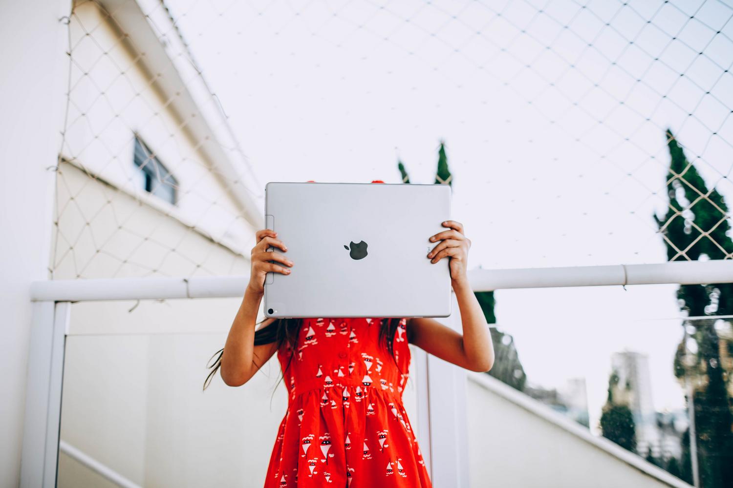 Menor ocultando su rostro detrás de una tablet, ilustrando la importancia de la privacidad online y la protección de la identidad digital infantil.