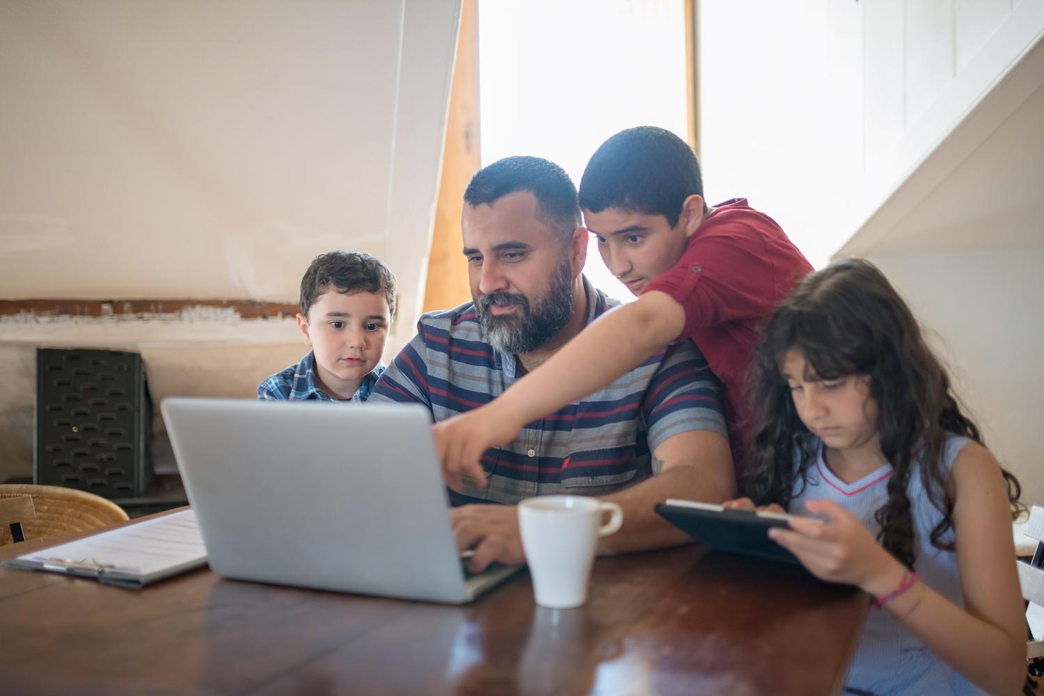 Padre acompañando a sus hijos mientras utilizan un ordenador portátil en casa, representando la educación digital y el papel fundamental de la familia.