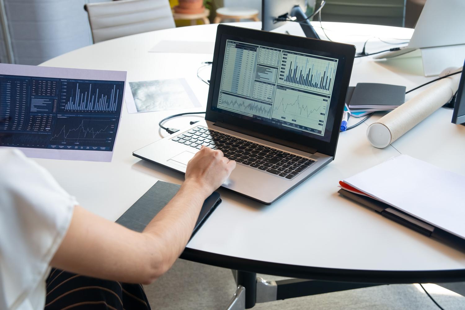 Persona analizando gráficos financieros en un portátil en una oficina moderna, ilustrando la optimización de datos en Excel.