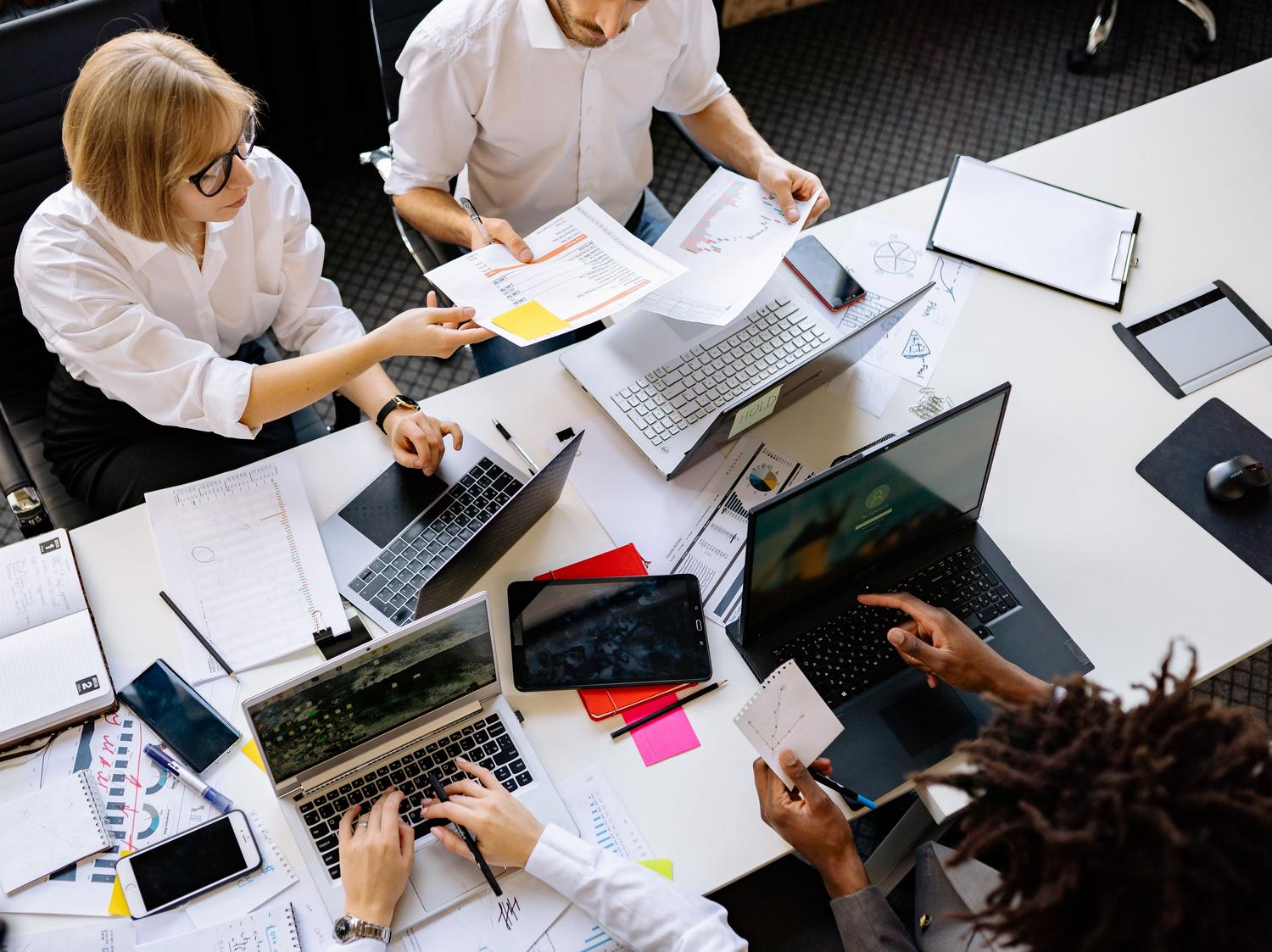 Vista superior de un equipo diverso colaborando en una oficina con portátiles y documentos, simbolizando las Páginas de Copilot.