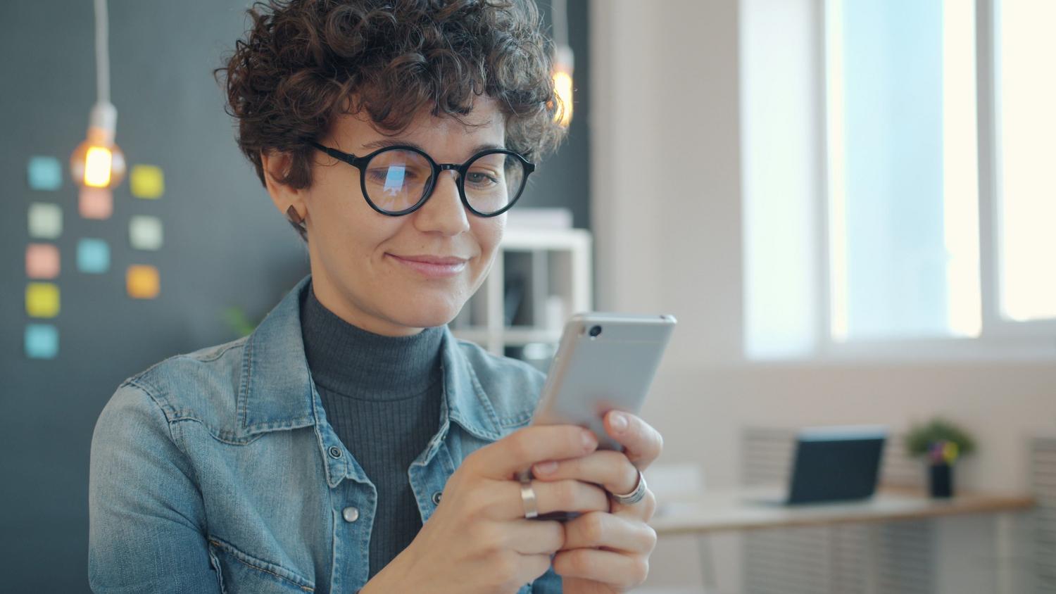 Mujer profesional usando su móvil en una oficina moderna, vinculada a la gestión de chats de trabajo y productividad.